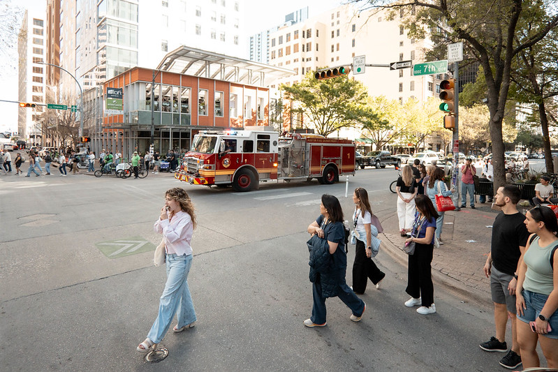 Young woman crossing 7th Street in Austin during SXSW 2026, fire truck passing in the background
