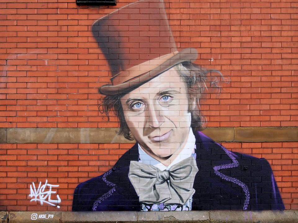 A street art mural of Willy Wonka in his felt hat painted on a wall in Denton, England