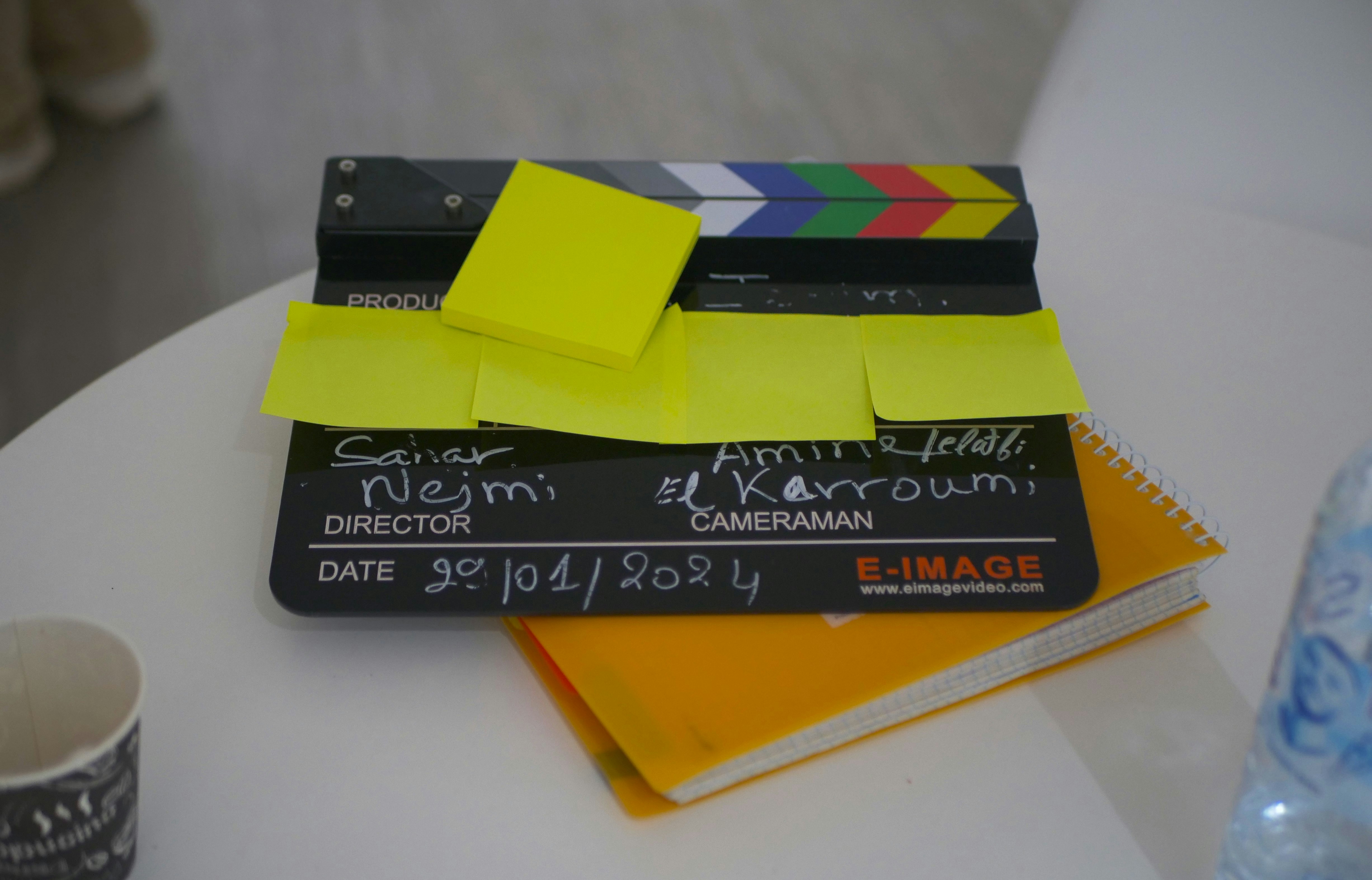 Clapperboard with yellow sticky notes and a notebook on a table